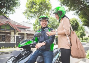 woman standing sidewalk ordering commercial motorcycle taxi scaled